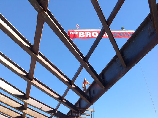 The signed beam, with its banner, flag and tree, are lifted into place at the Broad topping out.